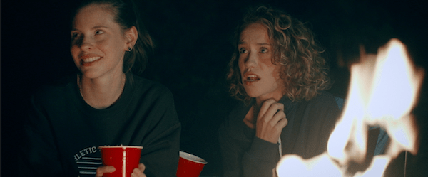 Two characters sit next to a camp fire in Camping Trip